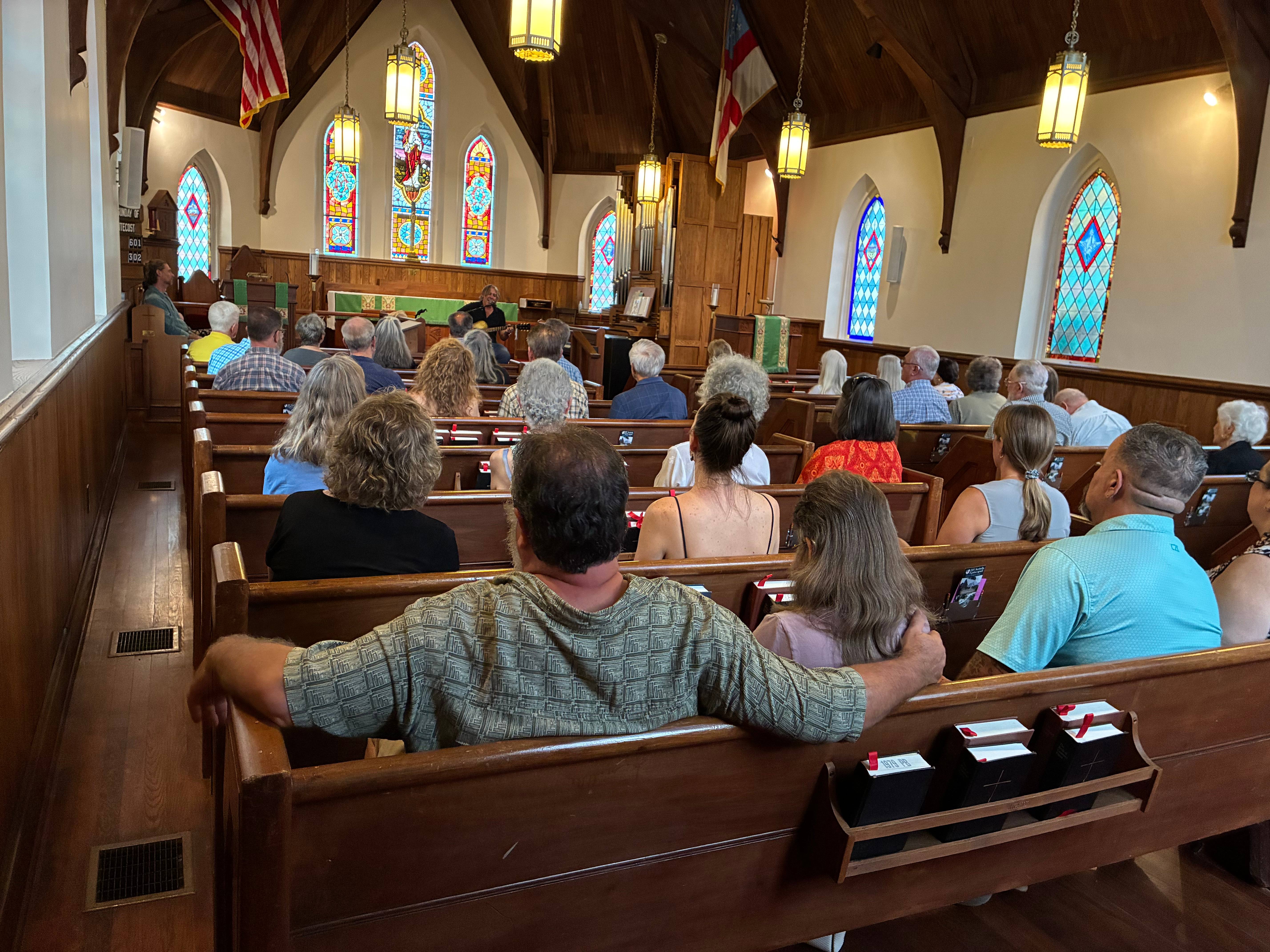 The chapel filled with guests in the pews as a performer plays at the front beneath the stained-glass windows