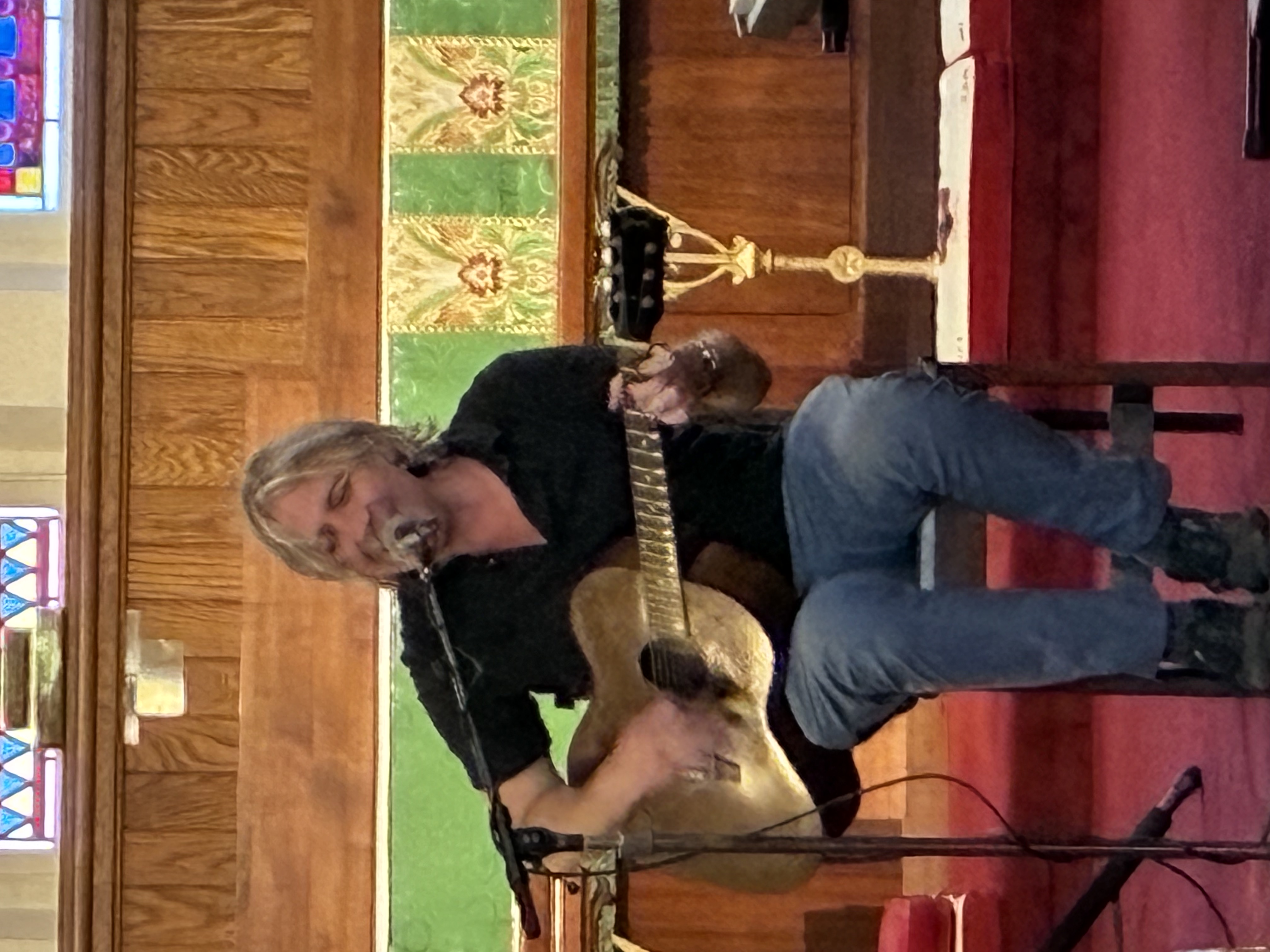 Jamie Rasso singing into the microphone while playing acoustic guitar during the concert