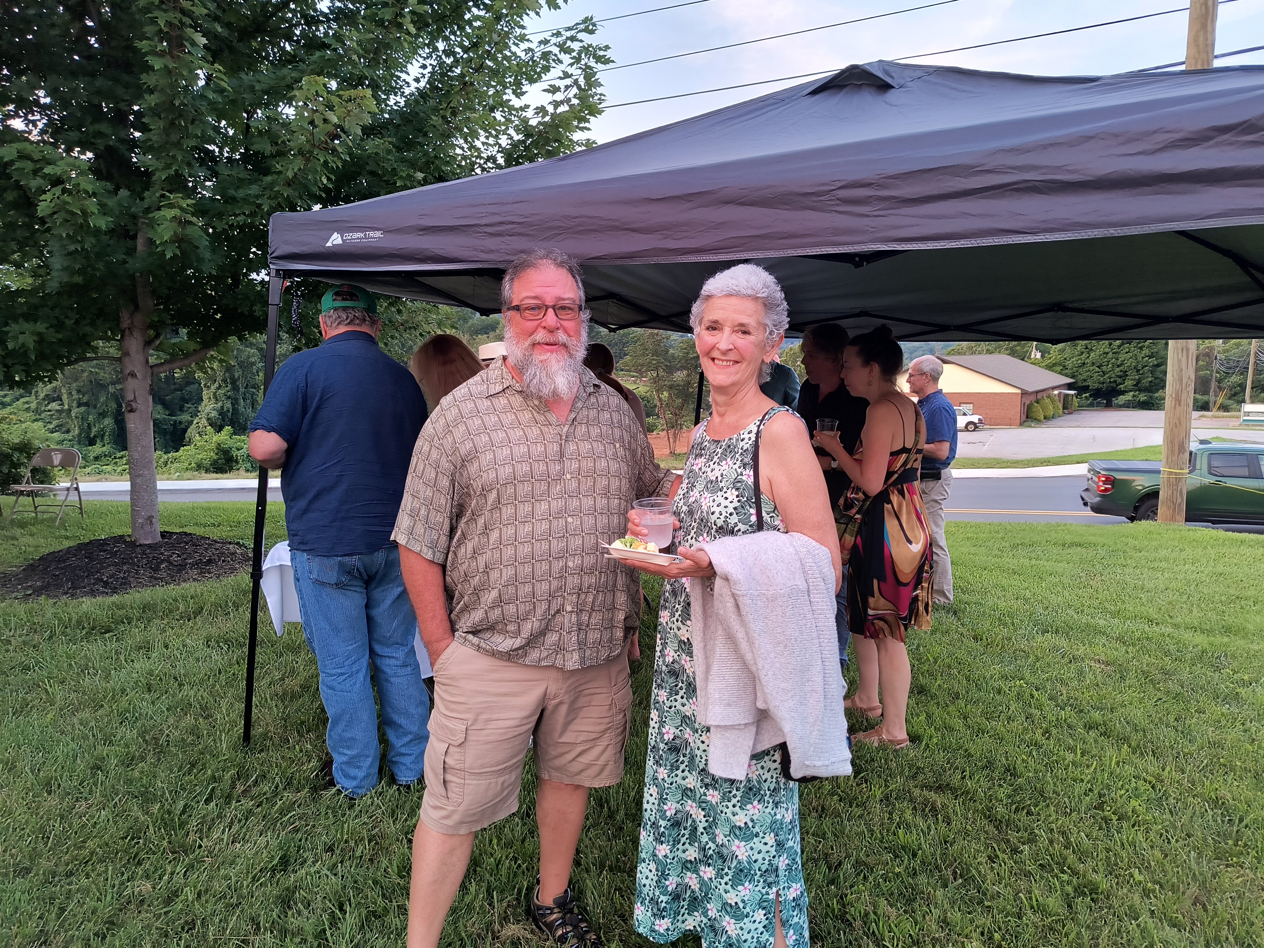 A smiling couple under the canopy tent, the reception in full swing behind them