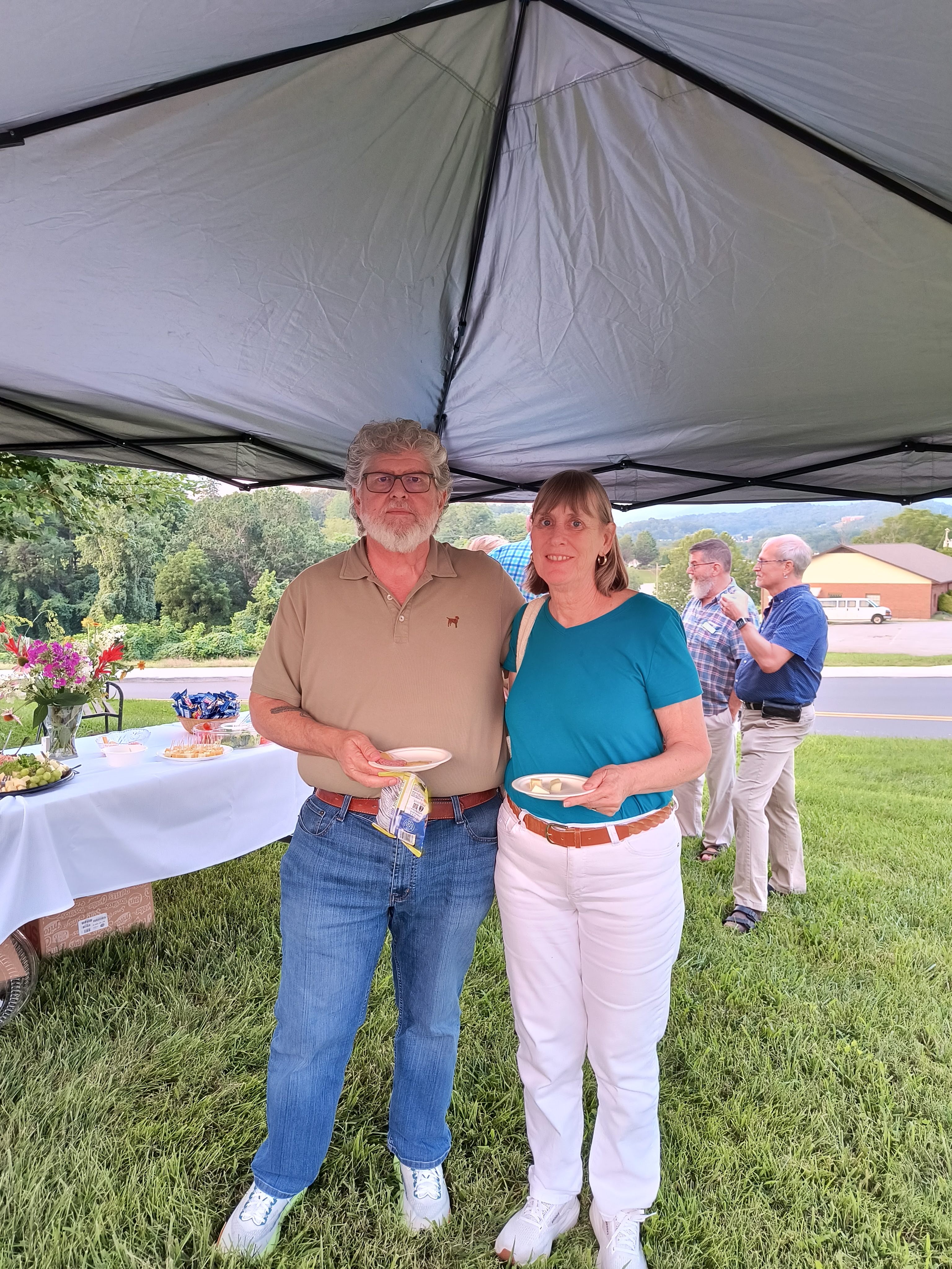A couple enjoying plates of food under the canopy tent at the reception