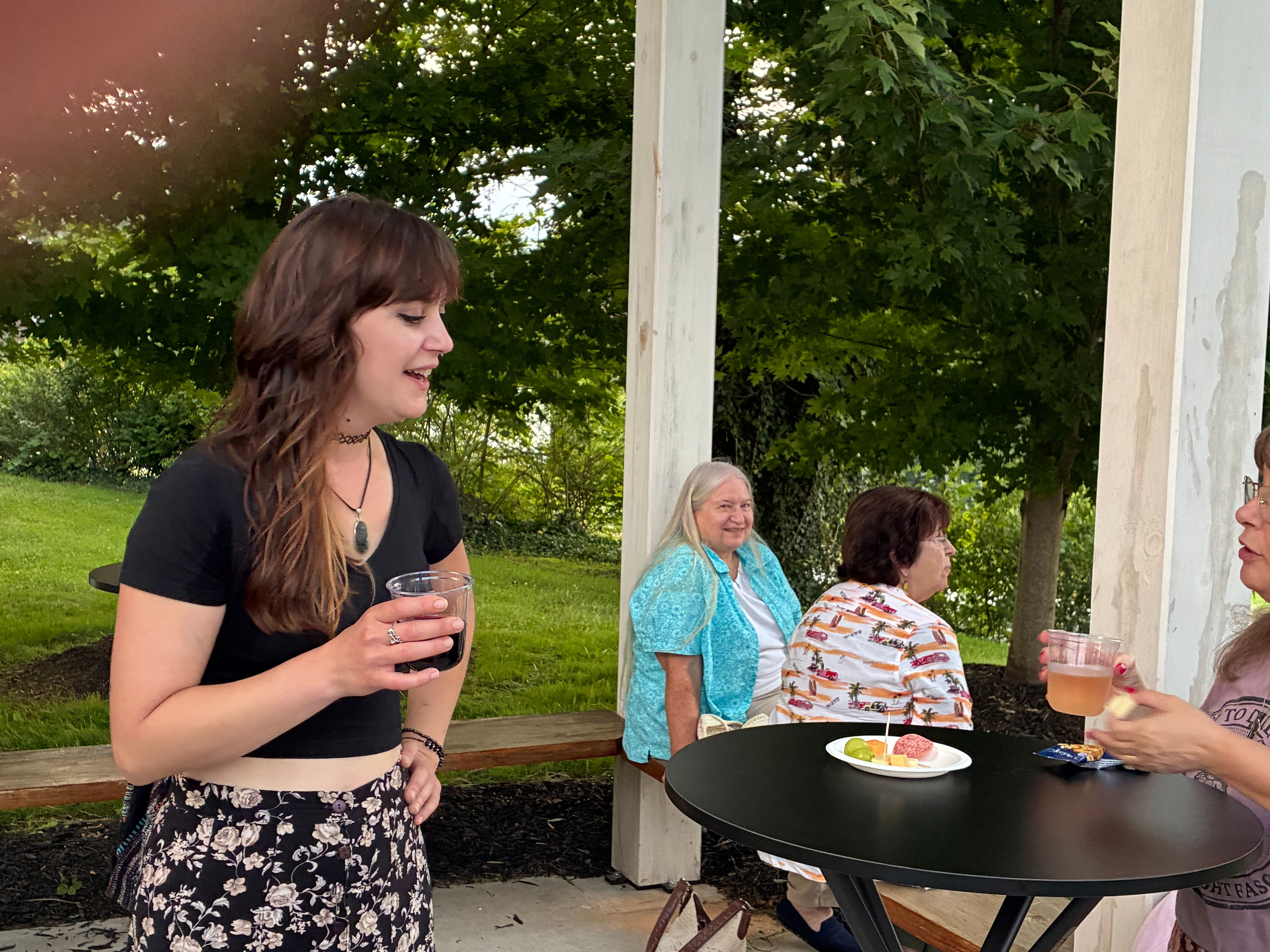 A guest with a drink sharing a laugh in conversation under the Arbor pergola while others sit together nearby
