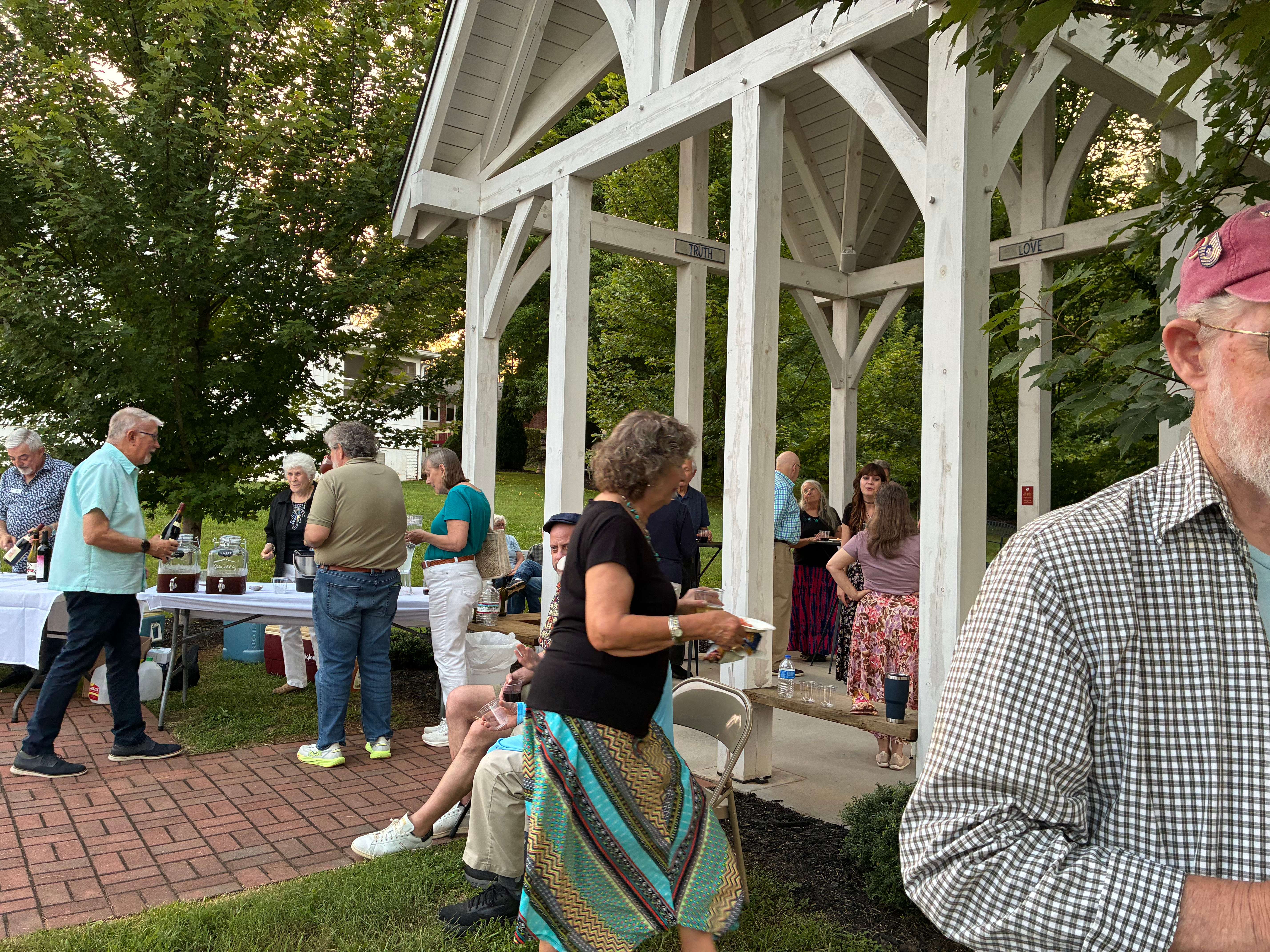 Members enjoying fellowship by the white Arbor pergola and the beverage table