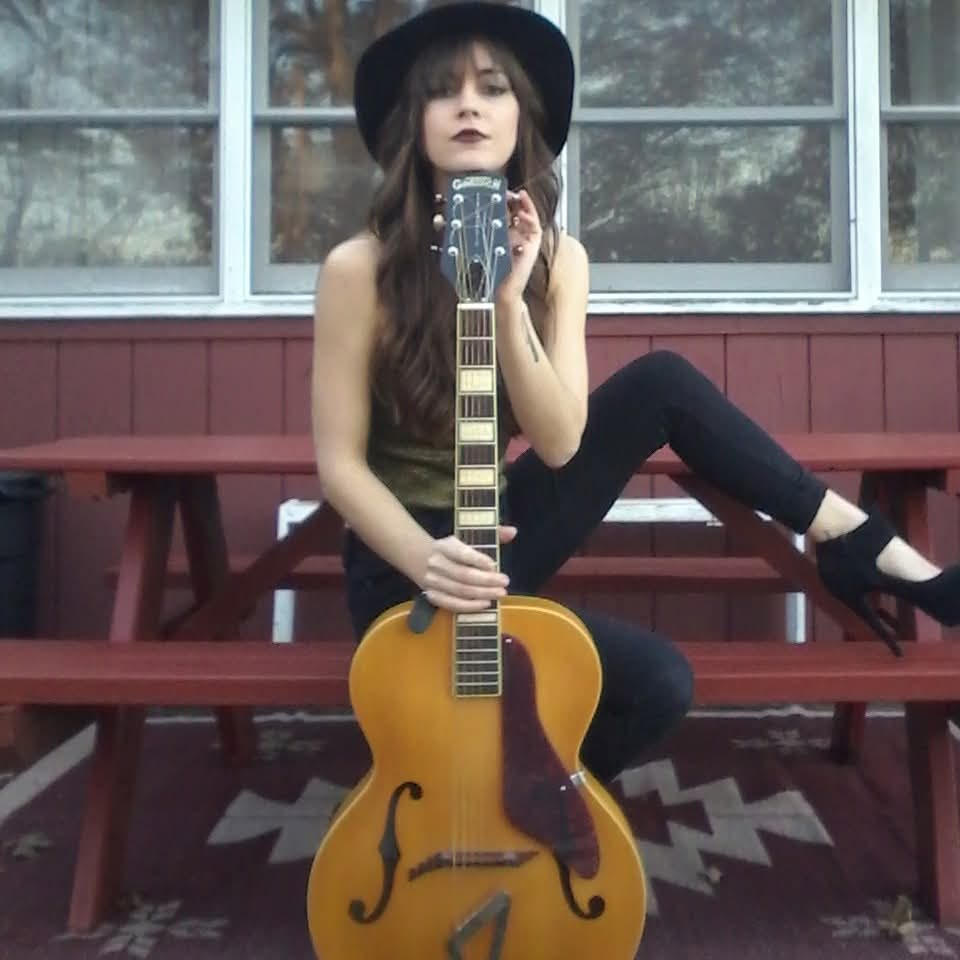 Diana New wearing a black hat and holding a vintage archtop guitar