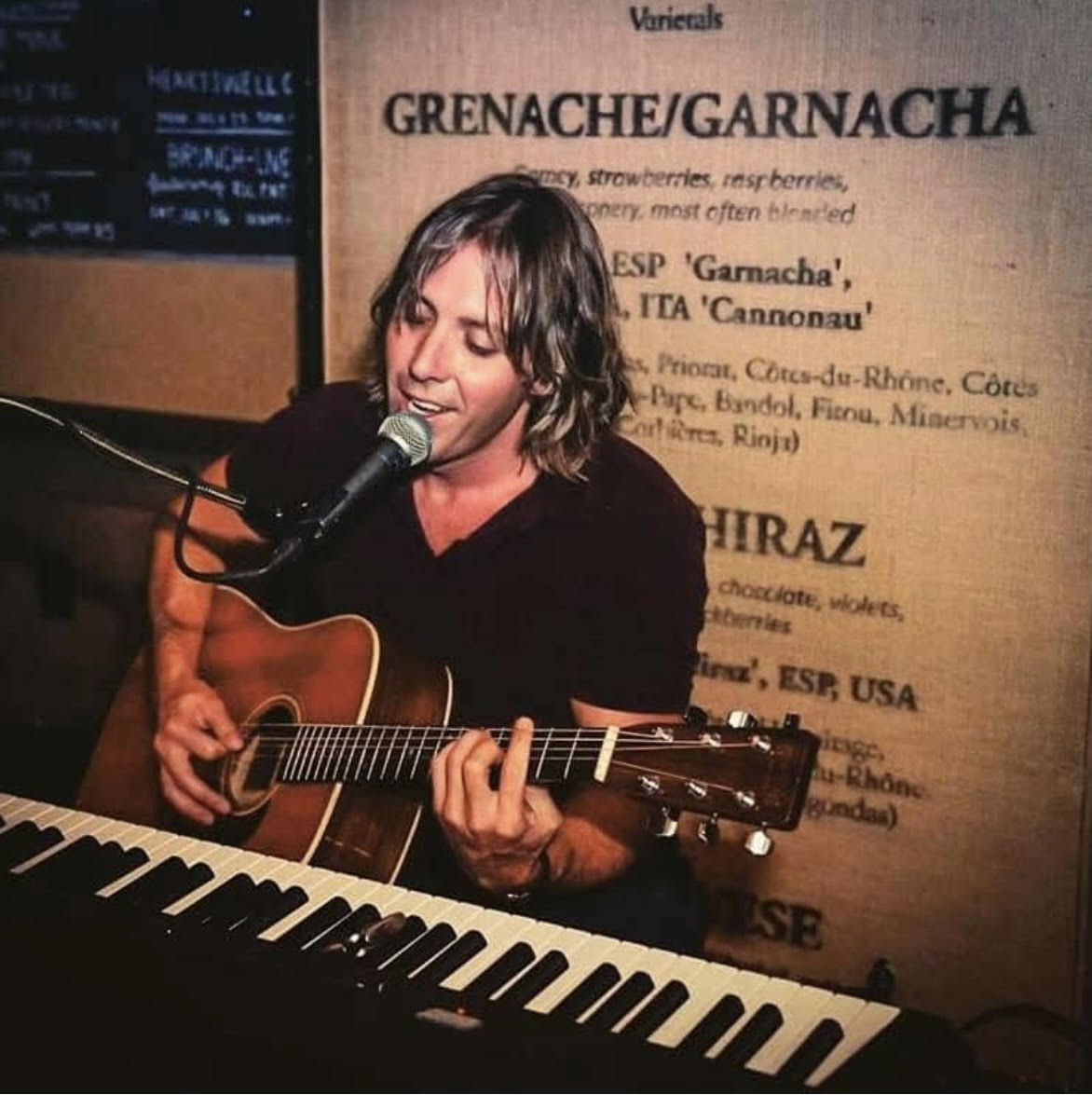 Jamie Rasso singing into a microphone while playing acoustic guitar