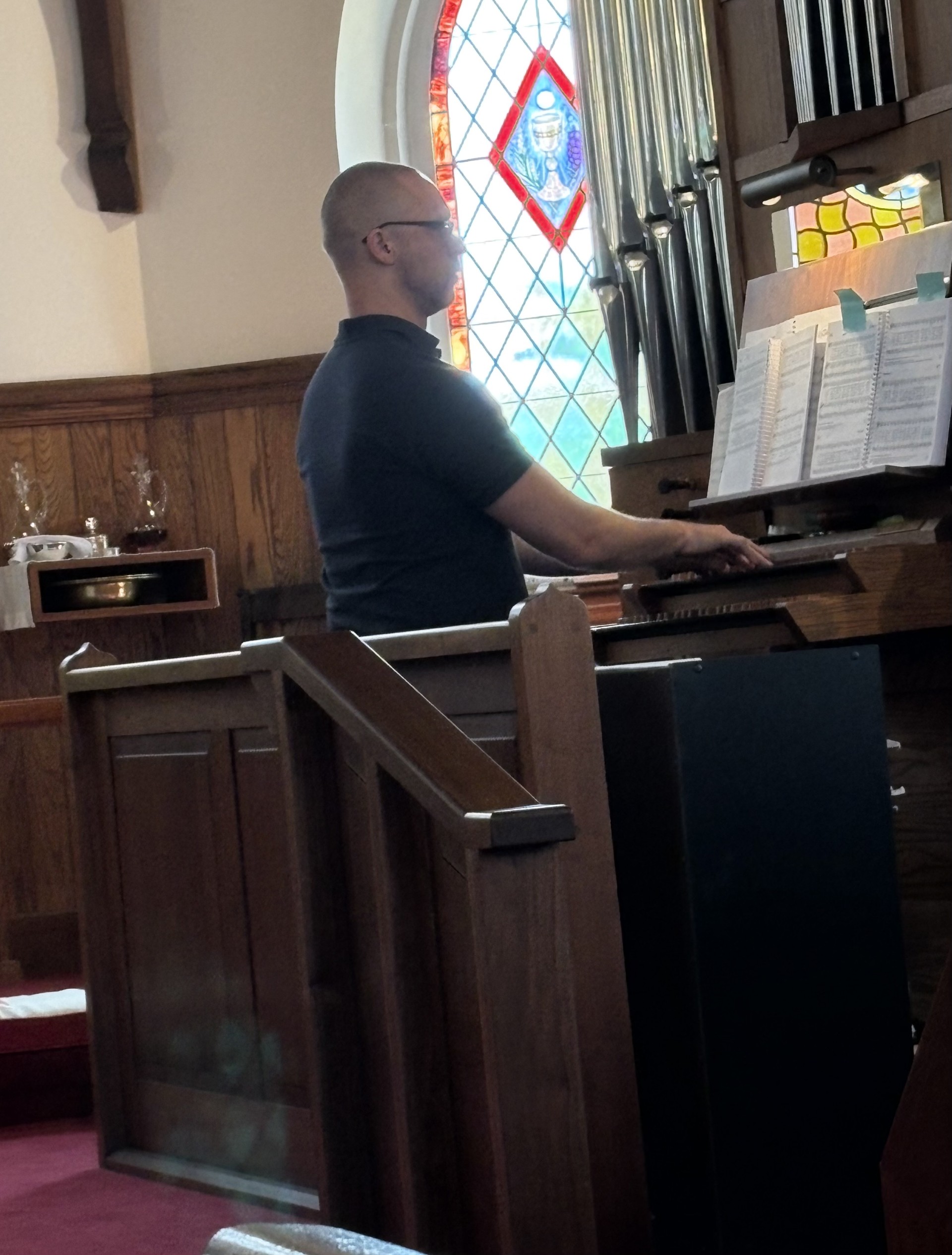 Organist playing the pipe organ beside a stained glass window