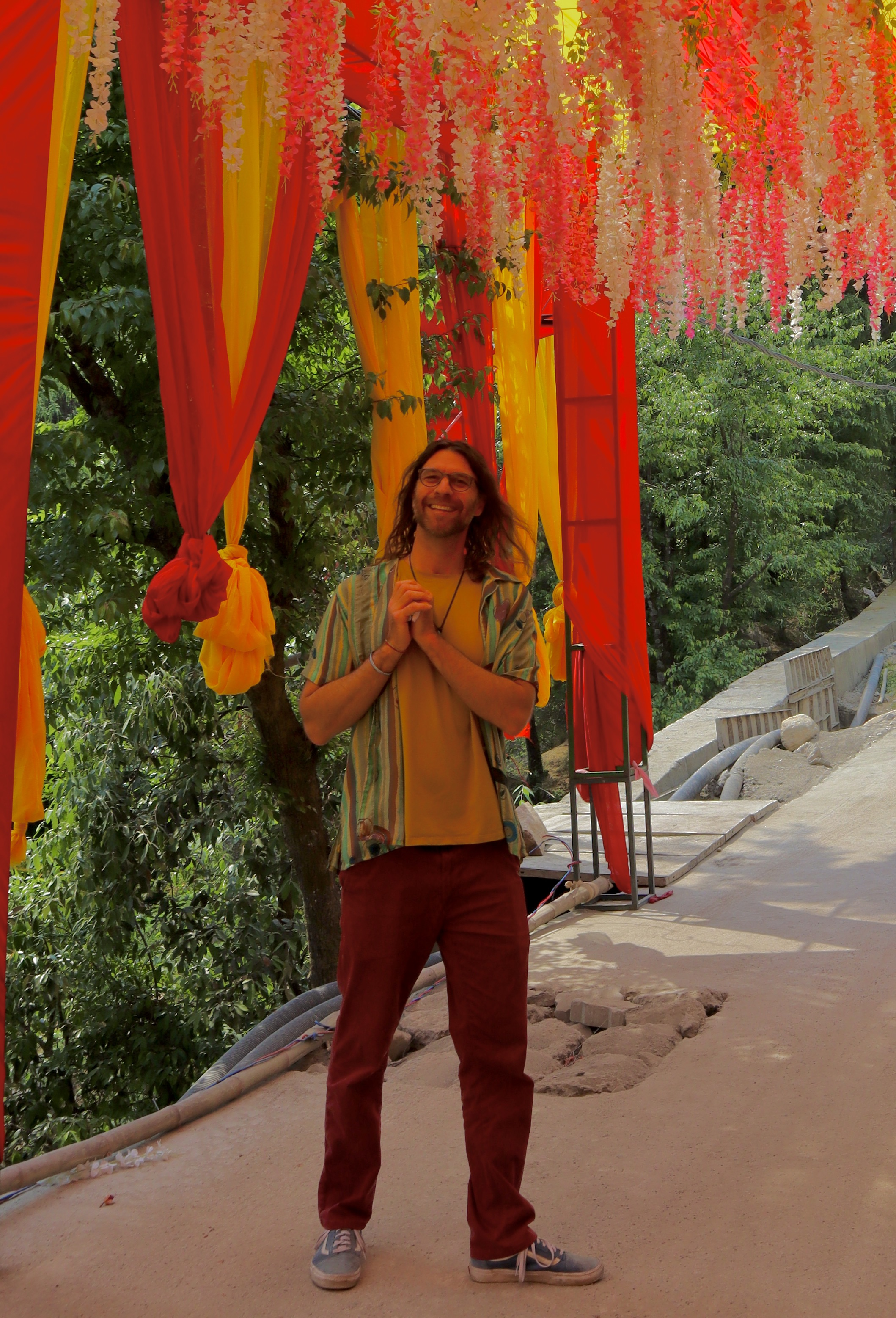 Brian Van Fleet smiling with his hands clasped, standing beneath colorful draped fabrics and floral garlands